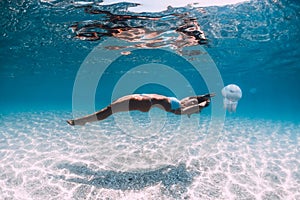 Woman underwater over sandy sea with jellyfish. Freediving in blue ocean