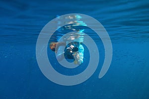 Woman with underwater photo camera swimming in sardines colony. Open water of deep blue ocean. Snorkeling in open sea