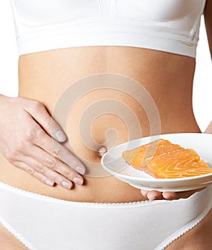 Close Up Of Woman In Underwear Holding Plate Of Salmon And Touching Stom photo