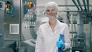Woman in uniform smiles, while standing in a dairy factory room.