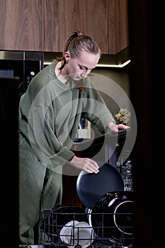 Woman unloading clean dishes from dishwasher at home