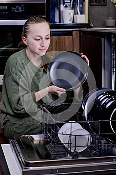 Woman unloading clean dishes from dishwasher at home