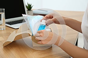 Woman unpacking box with antiseptics and respiratory masks at wooden table, closeup. Protective essentials during COVID-19