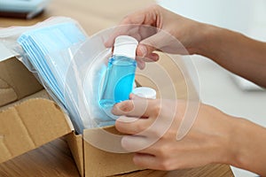 Woman unpacking box with antiseptics and respiratory masks at wooden table, closeup. Protective essentials during COVID-19