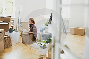 Woman unpacking stuff from carton boxes on the floor while moving-in