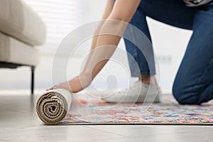 Woman unrolling carpet with beautiful pattern on floor in room, closeup