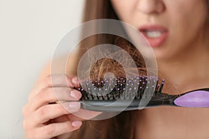 Woman untangling her hair from brush on light background