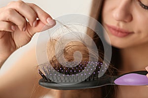 Woman untangling her hair from brush on light background