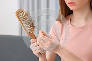 Woman untangling her lost hair from brush indoors, closeup. Alopecia problem