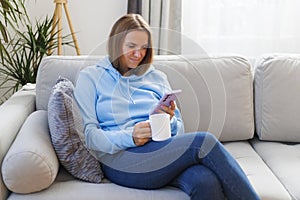 A woman unwinds on a comfortable sofa, smartphone in hand, and a cup of tea