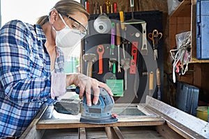 Mature Woman Upcycling Furniture In Workshop At Home Using Electric Sander photo