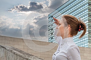 Woman on urban background looking ahead at sun between clouds in sky