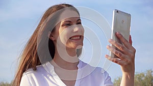 Woman use mobile against blue sky. Smiling female talking with friends via cellphone in slow motion