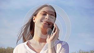 Woman use mobile against blue sky. Smiling female talking with friends via cellphone in slow motion