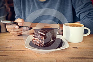 Woman use mobile phone with coffee cup and chocolate cake on wood table in coffee shop.