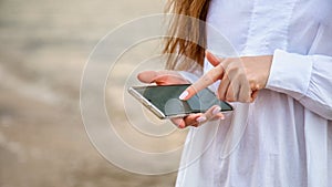 Woman use mobile phone to search in internet or check app outside. Closeup female hands with smartphone rest at sea water