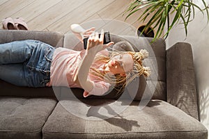 Woman use a smartphone while lying on a sofa. Top view