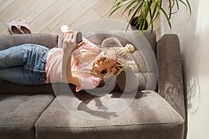 Woman use a smartphone while lying on a sofa. Top view