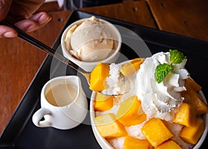 Woman use spoon take shaved ice dessert, served with mango sliced.  Served with vanilla ice cream and whipped cream