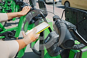 Woman uses app in her smartphone to rent a shared electric bike for a trip around the city. Solving the problem of transport in