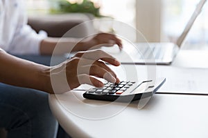 Woman uses calculator and laptop seated at table, close up