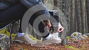 Woman uses gas burner to warm tea in forest camping having break during hiking.