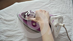 Woman uses hot iron on white fabric sheet on ironing board