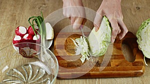 A woman uses a kitchen knife to cut fresh white cabbage on a wooden cutting board. Close-up female hands chopping