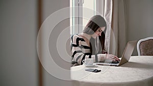 Woman uses laptop and enjoying morning coffee on a bright dining. slider to the right, view through the open doors