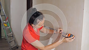 A woman uses a measuring tape measure to measure the wall for wallpapering.