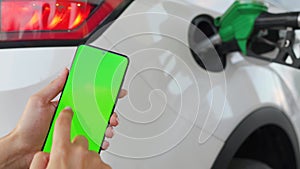 Woman uses a mobile application in a smartphone to pay for refueling a car. Smartphone with a green screen. Chroma key