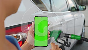 Woman uses a mobile application in a smartphone to pay for refueling a car. Smartphone with a green screen. Chroma key