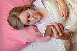 Woman uses mobile phone in a bed. Middle aged 40 years woman lying on pillow and read on smartphone. Social networking or internet