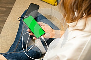 The woman uses a mobile phone, a smartphone with green screen, charged from the power bank