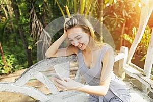 Woman uses smart phone on sunny day, background of sunshine green palms in Thailand, Phuket