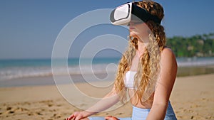 Woman uses VR headset for beach meditation, virtual reality transports to serene environment, relaxation tech trend