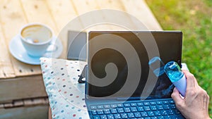 Woman using alcohol nano mist sprayer cleaning a laptop to prevent the virus and bacterias in garden. Quarantine for coronavirus