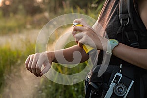 Woman using anti mosquito spray outdoors at hiking trip. Close-up of young female backpacker tourist applying bug spray on hands