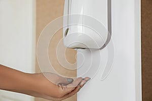 Woman using automatic hand sanitizer dispenser indoors, closeup