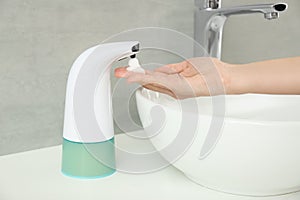 Woman using automatic soap dispenser in bathroom