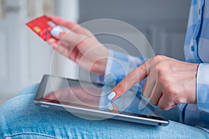 Woman using black tablet and red credit card for online shopping at home