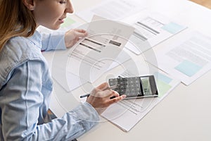 Woman using calculator and holding documents in hands