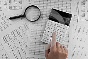 Woman using a calculatorwith magnifyingglass and financial statement lying on the table