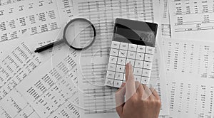 Woman using a calculatorwith magnifyingglass and financial statement lying on the table