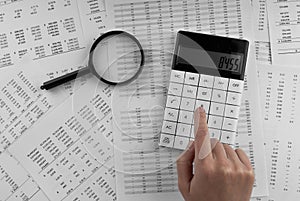 Woman using a calculatorwith magnifyingglass and financial statement lying on the table