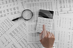 Woman using a calculatorwith magnifyingglass and financial statement lying on the table