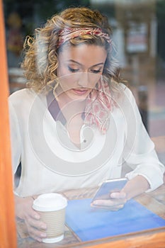 Woman using cell phone in cafe seen through window