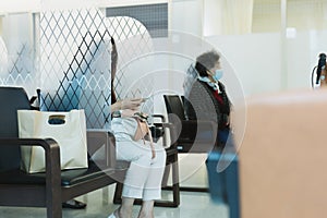 Woman using cell phone sitting in partition while wating in hospital covid-19 pandemic.