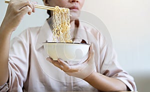 Woman using chopsticks eating instant ramen, noodles, cheap food and no money for dinner