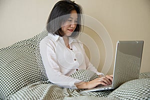 Woman using computer laptop while wake up on bed in the morning